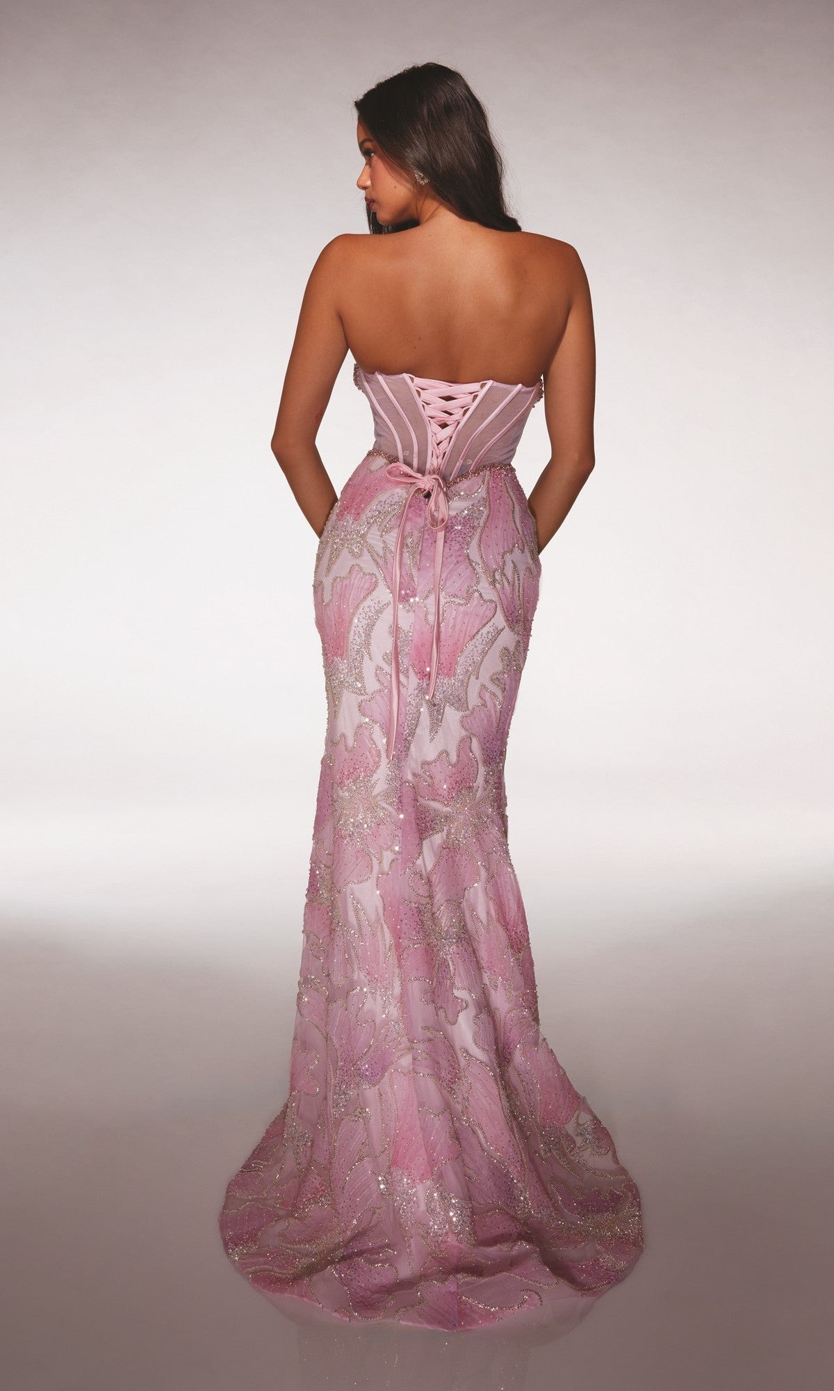 A woman faces away, wearing the Alyce 62187 long prom dress featuring a strapless, floor-length design with a sheer corset bodice, lace-up back, and delicate floral lace details.